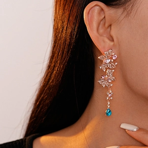 Detail of elegant gold drop earrings with pink crystals and a deep blue teardrop gem