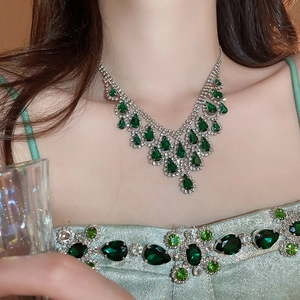 Detail of silver V-shaped necklace with green teardrop stones and clear diamonds on model