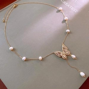 Detail of gold butterfly necklace with zircons and pearls on dark green book cover