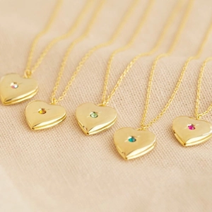 Golden heart locket necklaces with colorful birthstones on beige linen background