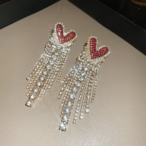 Close-up of red rhinestone heart earrings with long sparkling crystal tassels on a board
