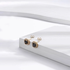 Boucles d'oreilles dorées géométriques avec pierre noire et diamants sur fond blanc