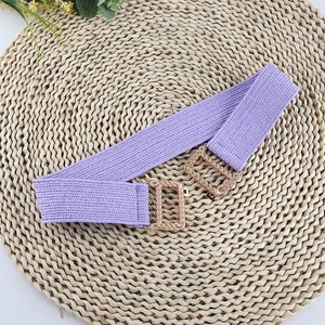 Detail of purple elastic woven belt with golden textured metal buckle on straw mat