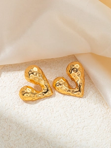 Detail of gold irregular heart earrings with hammered metal texture on stone surface