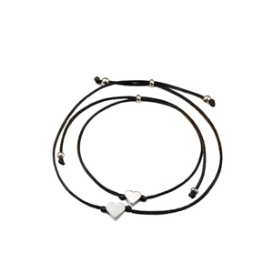 Détail de deux bracelets tissés noirs avec pendentifs en cœur argentés sur fond blanc
