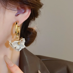 Close-up of golden floral stud earring with ivory petals worn by model on ear