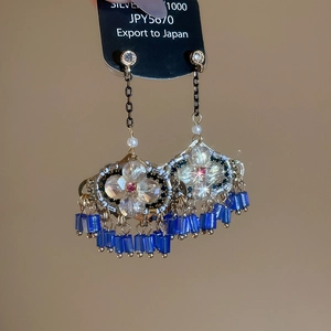 Détail de boucles d'oreilles bohèmes avec fleurs en cristal et pompons bleus dorés