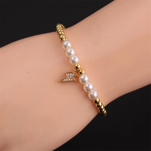 Gold beaded pearl bracelet with zircon lightning bolt charm worn on a female wrist