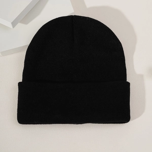 Close-up of a black knitted beanie with a wide cuff on a minimalist white surface