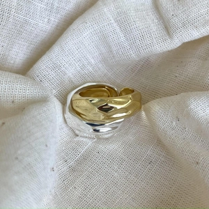 Detailed close-up of textured gold and silver irregular hammered metal rings on white fabric