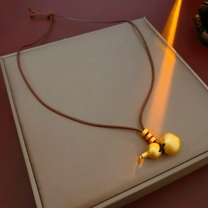 Detailed view of golden gourd pendant with brown cord and red decorative beads