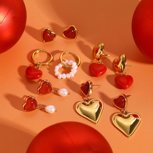 Goldene Herz-Ohrringe und Perlenring-Set mit roter Emaille auf warmem orangefarbenem Grund