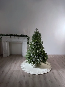 Detail of white knit Christmas tree skirt with festive cable pattern on a green tree