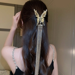 Détail d'une pince à cheveux papillon dorée avec de longs glands en strass brillants