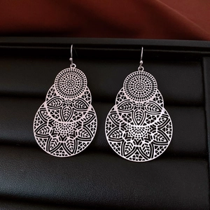 Detail showing silver hollowed leaf earrings with a triple-tier floral design on leather