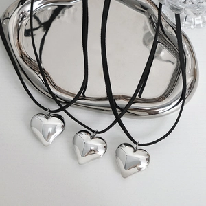 Set of three polished heart pendant necklaces with black cords on a silver tray