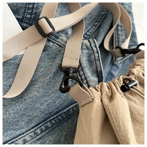 Detail der beigen Nylon-Kordelzugtasche mit schwarzer Schnalle auf blauem Denim