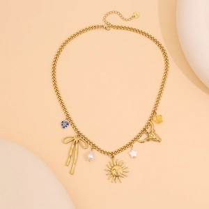 Détail du collier à grosse chaîne dorée avec cœur bleu, nœud et breloques sur fond beige