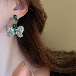 Close-up of model wearing silver butterfly earrings with green emeralds and diamonds
