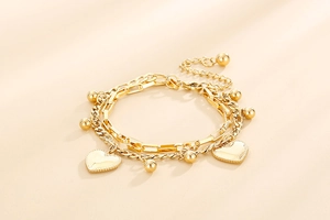 Detail of gold double-layer bracelet featuring heart pendants and small round beads
