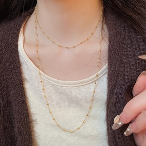 Close-up of a double-layered gold bead chain necklace on a brown sweater