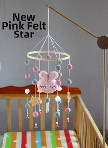 Detail of baby crib mobile with plush pink bunny, felt star, and colorful pom-poms