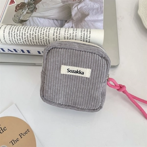 Detail view of grey corduroy makeup pouch with pink strap and metal zipper on white desk
