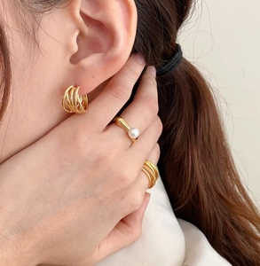 Detail of model wearing gold multilayer hoop earrings and minimalist pearl ring set