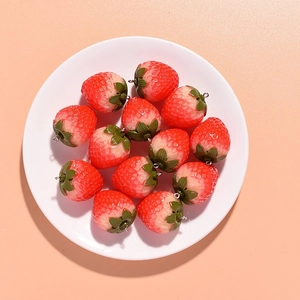 Close-up of red and white resin strawberry pendants with metal hooks on a white plate