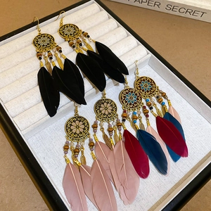 Bohemian feather tassel earrings with gold floral circles and beads displayed on a tray