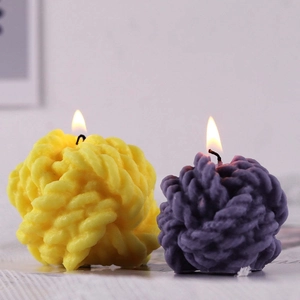 Ball of yarn scented candles in yellow and purple showing woven texture and lit wick
