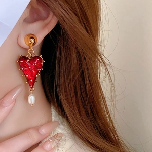Detail of gold heart earrings with red enamel and a small white pearl on model