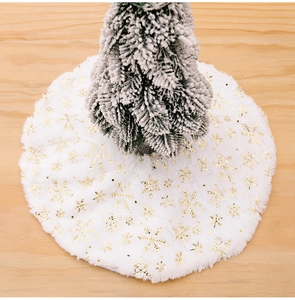 Detail of white plush Christmas tree skirt with golden snowflake patterns on wood floor