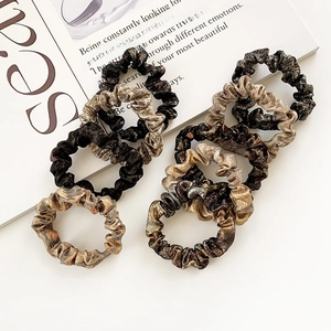 Set of eight velvet hair scrunchies in black, brown, and gold colors on a white magazine