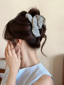 Detail of grey pleated fabric hair claw clip styled on a low bun hairstyle
