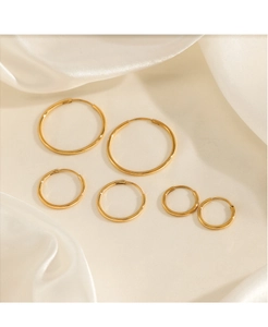 Three pairs of polished gold hoop earrings in various sizes on soft white silk fabric