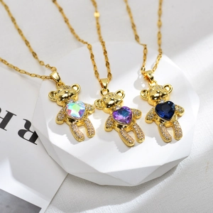Three gold teddy bear necklaces with sparkling heart crystals on a white marble stand