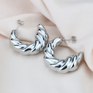 Detailed view of silver twisted hoop earrings on soft beige silk fabric background
