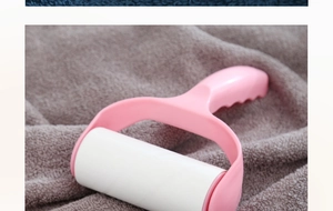 Close-up of a pink lint roller with a white sticky roll on dark grey plush fabric
