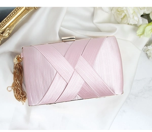 Close-up of pink satin evening clutch with elegant gold tassels on white silk fabric
