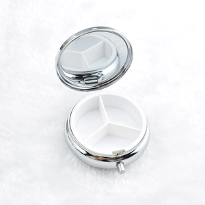 Detail view of round metal pill box with three compartments and interior mirror