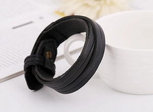 Detail shot of multi-layer black leather bracelet with metal clasp on a wooden desk