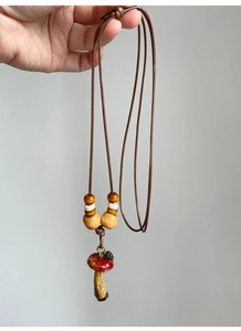 Detail of red mushroom pendant with wooden beads on adjustable brown woven cord necklace