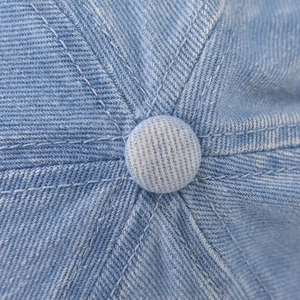 Macro detail of high-quality stitching and top button on washed denim baseball cap
