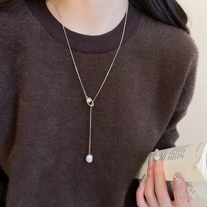 Close-up of a long golden Y-shaped necklace with a pearl drop on a brown sweater