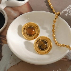 Close-up of vintage golden earrings featuring brown tiger eye stones in a white bowl
