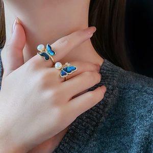 Close-up of gold butterfly rings with blue shell wings and freshwater pearls on model