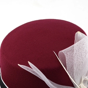 Dettaglio cappello in feltro bordeaux con elegante rete bianca e decorazione con piume