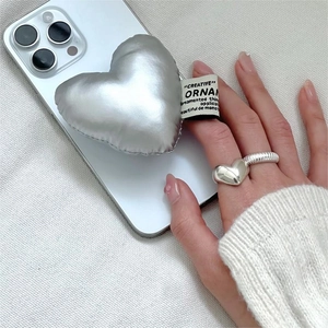 Polished silver heart phone grip and matching metallic heart ring on white fabric