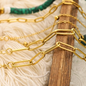 Macro shot of golden paperclip chain with green and white beads on a soft knit background